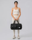 Model holding a black FlowHold Carry Bag in front with both hands styled for everyday movement