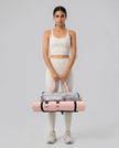 Woman holding a pink and gray Flow Hold Carry Bag with a yoga mat inside on a neutral studio setting