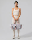Model holding a gray FlowHold Carry Bag in front with both hands styled for everyday movement