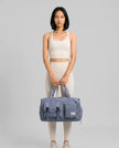 Model holding a light indigo FlowHold Carry Bag in front with both hands styled for everyday movement