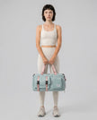 Model holding a turquoise FlowHold Carry Bag in front with both hands styled for everyday movement