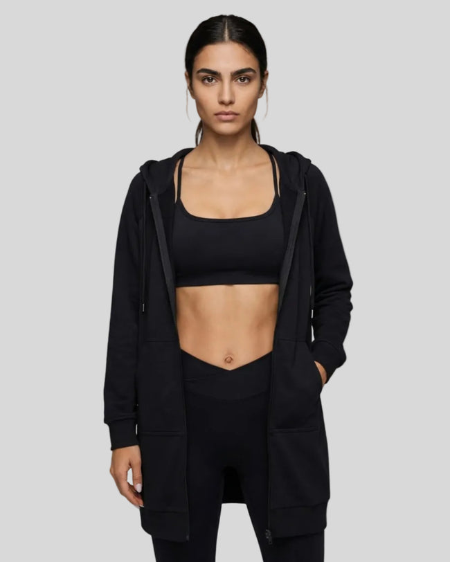 Model wearing a black longline hoodie open front styled with activewear in minimal studio setting