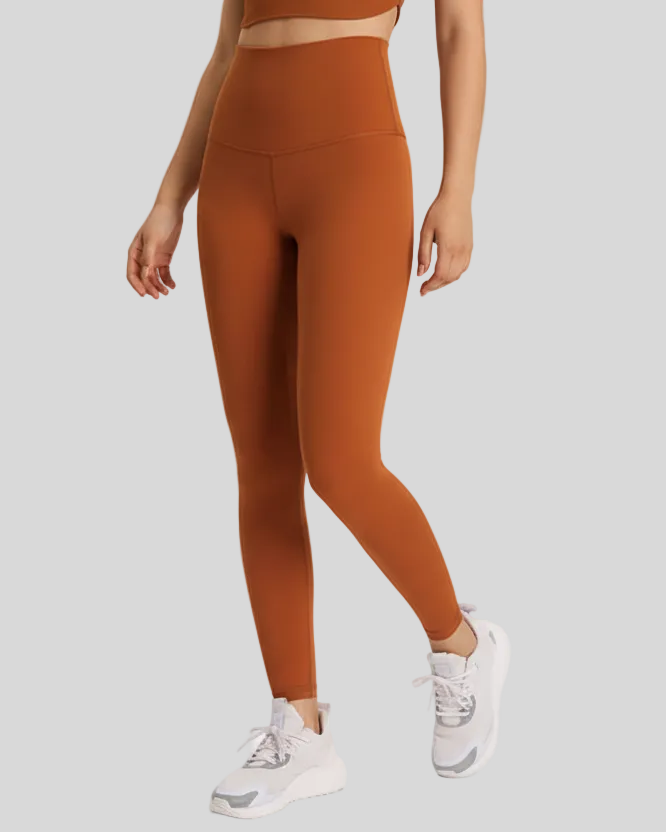 Woman wearing brown-colored FlowLine Hold Soft leggings and white sneakers on a light gray background