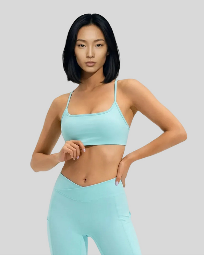 Model wearing an aqua LumaForm Crisscross sports bra and leggings on a light gray background