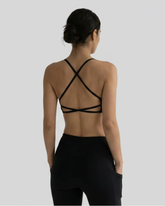 Model wearing a black LumaForm Crisscross Sports Bra and leggings against a neutral setting background