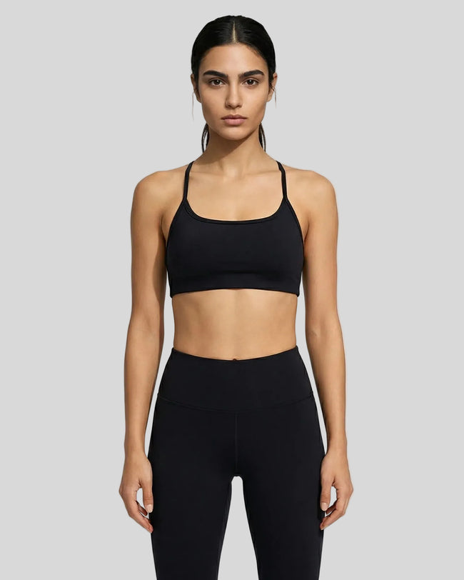 Model wearing a black LumaForm Crisscross sports bra and leggings on a neutral setting background