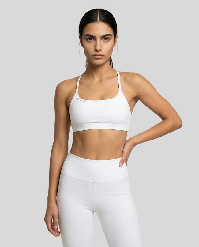 Model wearing a white LumaForm Crisscross sports bra and leggings on a light gray background
