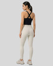 Full body back view of model wearing a black LumaForm Cross-Neck Cami and ivory leggings on a neutral setting