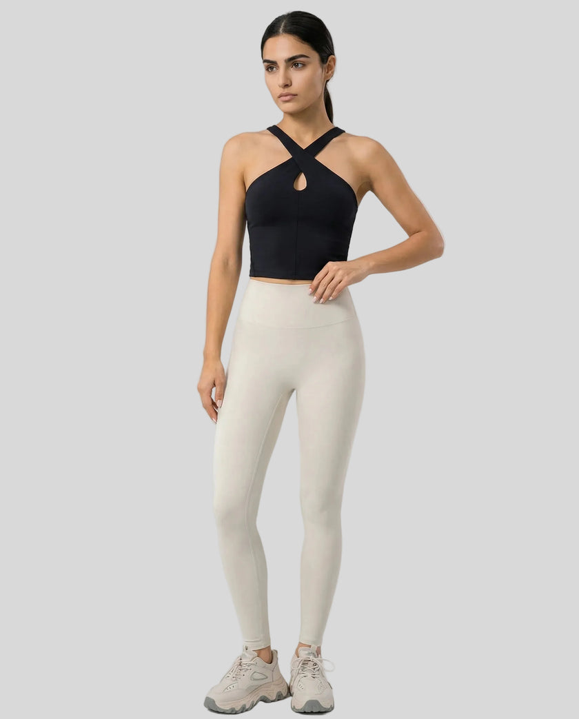 Full body front view of model wearing a black LumaForm Cross-Neck Cami and ivory leggings on a neutral setting