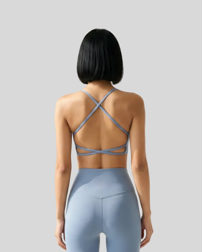 Back view of model wearing a dusty blue LuxeCrisscross Support Sports Bra in a neutral setting