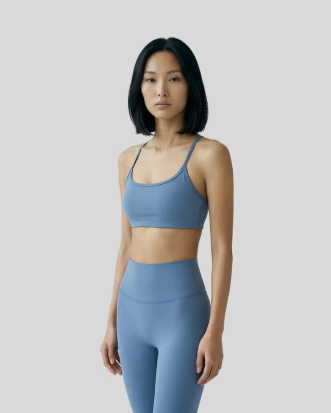 Model wearing a dusty blue LuxeCrisscross Support Sports Bra in a neutral setting