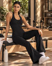 Woman wearing the MotionFlow Halter Jumpsuit in Black viewed from the front, sitting on yoga studio bench