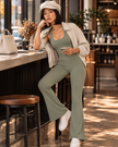 Woman wearing the MotionFlow Halter Jumpsuit in Gray Green styled with Axis Bomber Jacket and a paperboy hat, sitting in a coffee shop