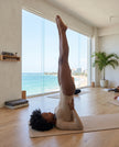 Model wearing the Athlesi MotionForm Long Sleeve Bodysuit in Khaki during a yoga pose, showing its flexible body-contouring fit