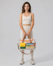 Model holding MotionPlay Travel Bag in beige styled for travel and everyday movement