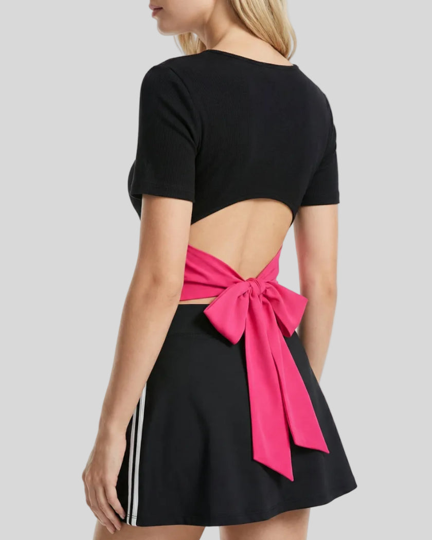 Angled upper body back view of woman wearing Nova Tie-Back Tee showing the open-back silhouette and Rose Red tie