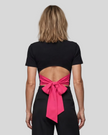 Upper body back view of woman wearing Nova Tie-Back Tee with open-back cutout and contrasting Rose Red bow