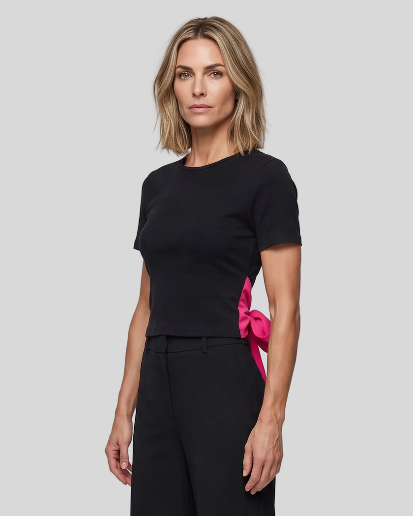 Angled upper body front view of woman wearing Nova Tie-Back Tee in black with contrasting Rose Red tie detail