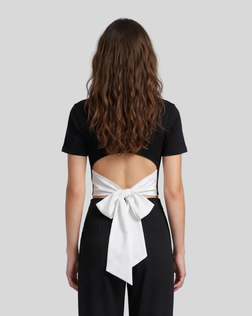 Upper body back view of woman wearing Nova Tie-Back Tee in black, with open-back cutout and contrasting White bow