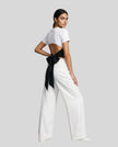 Angled full body back view of woman wearing Nova Tie-Back Tee in white, showing the open-back silhouette and Black tie