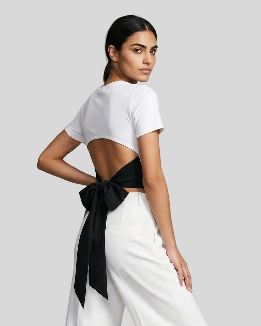 Angled upper body back view of woman wearing Nova Tie-Back Tee in white, showing the open-back silhouette and Black tie