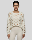 Mid body front closeup view of woman wearing white OpenWeave Cable Sweater with ivory leggings