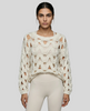 Mid body front closeup view of woman wearing white OpenWeave Cable Sweater with ivory leggings