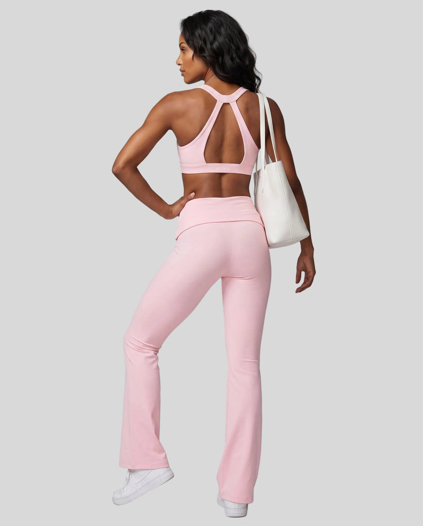 A woman modeling a pink Athlesi activewear set consisting of a Sculpt Halter Sports Bra with an open back and matching high-waisted flared Sculpt Yoga Pants