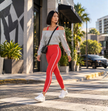 Woman wearing the Athlesi TrackLine Edge red activewear set with a Flower Gray off-shoulder hoodie, white sneakers, and black crossbody bag in an urban street setting