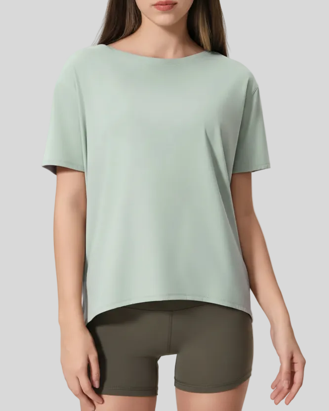 Woman wearing a light green softflow short sleeve top and olive green shorts on a gray background