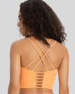 Woman wearing a sherbet sports bra with criss-cross back design on a light gray background
