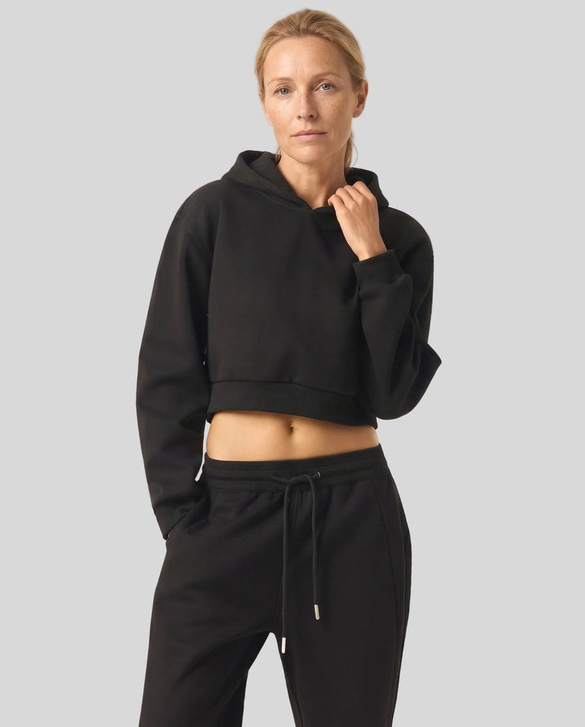 Angled front view of woman wearing black StudioEase Cropped Hoodie showing relaxed fit and cropped hem