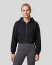 Upper body front view of woman wearing StudioEase Cropped Zip Hoodie zipped closed in Black