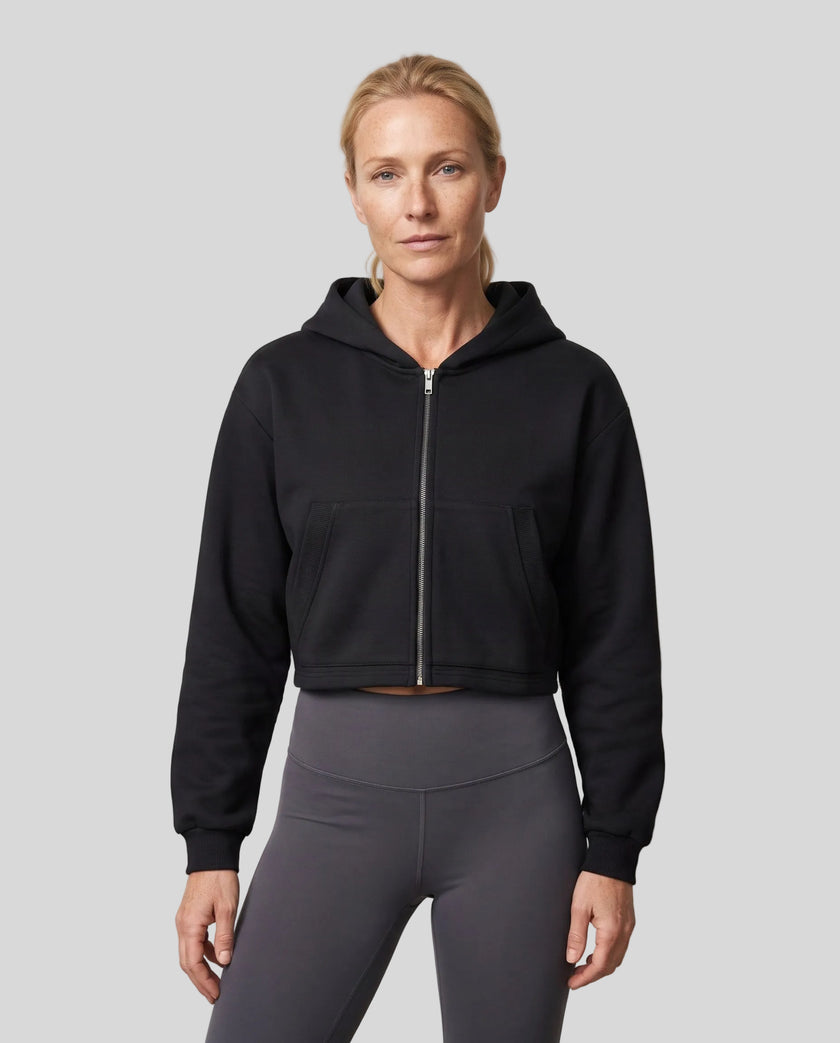 Upper body front view of woman wearing StudioEase Cropped Zip Hoodie zipped closed in Black