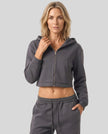 Upper body front view of woman wearing Charcoal Gray StudioEase Cropped Zip Hoodie zipped closed with matching sweatpants