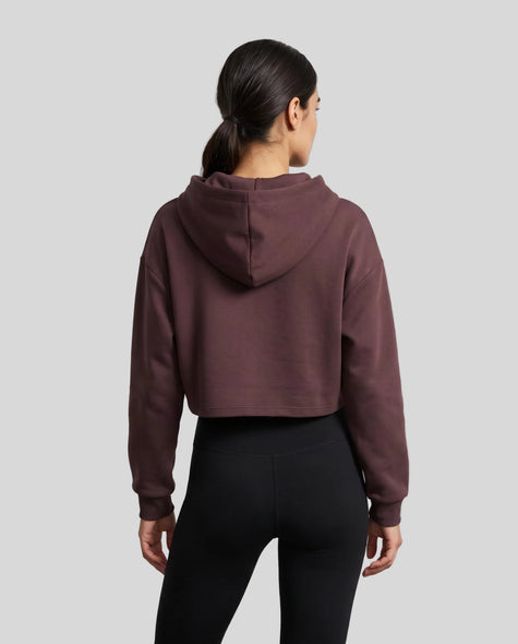 Upper body back view of woman wearing Dark Reddish Purple StudioEase Cropped Zip Hoodie showing hood and relaxed sleeves