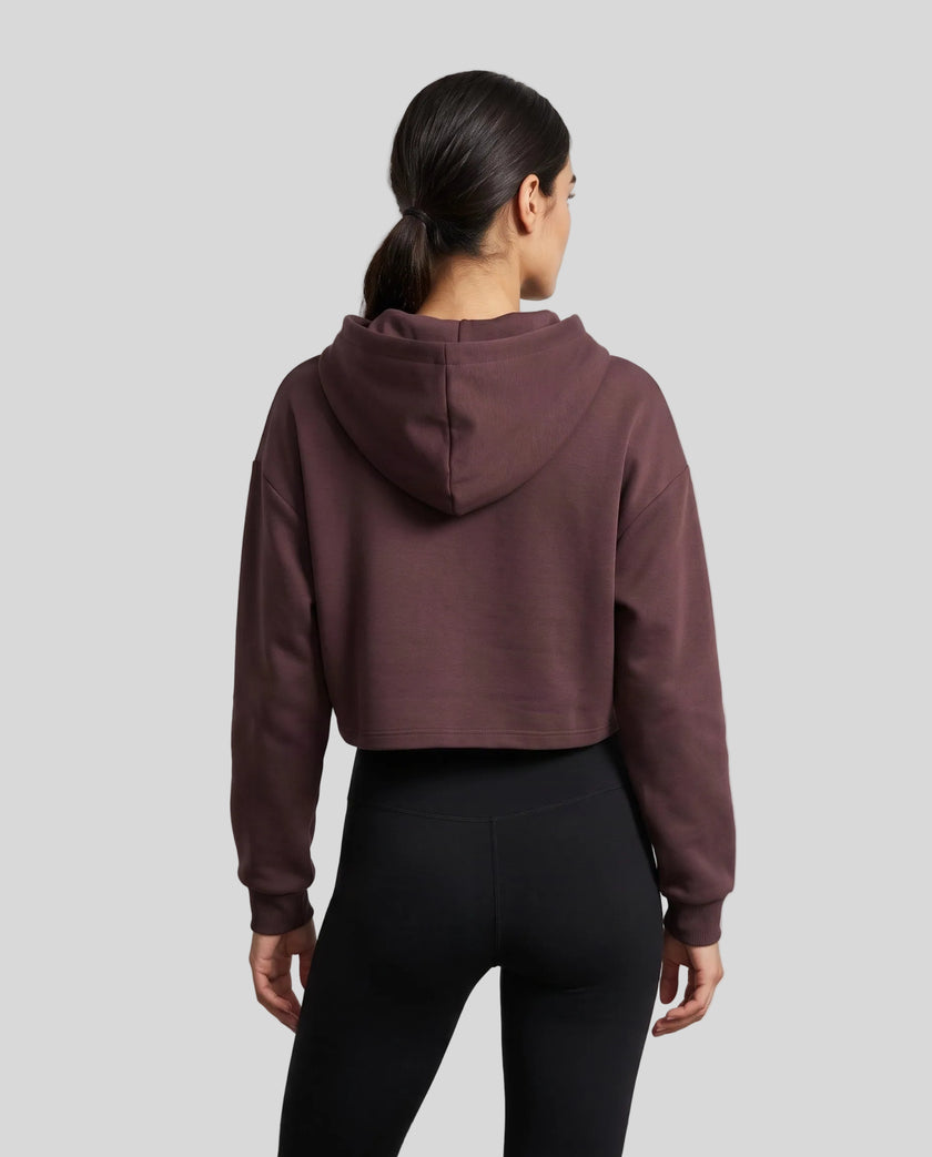Upper body back view of woman wearing Dark Reddish Purple StudioEase Cropped Zip Hoodie showing hood and relaxed sleeves