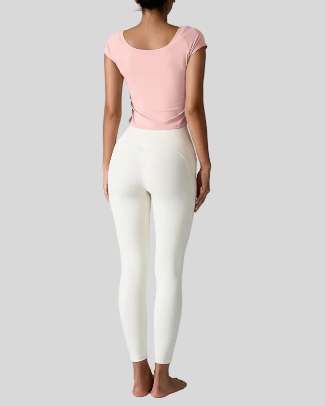Woman wearing a pink studioflow short sleeve active top and white leggings on a gray background