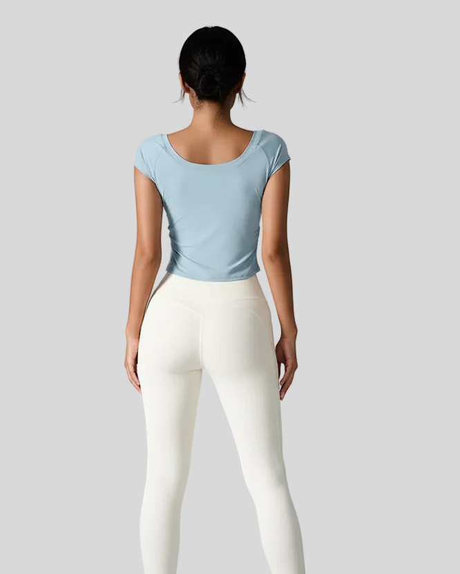 Woman wearing a light blue studioflow short sleeve active top and white leggings on a gray background