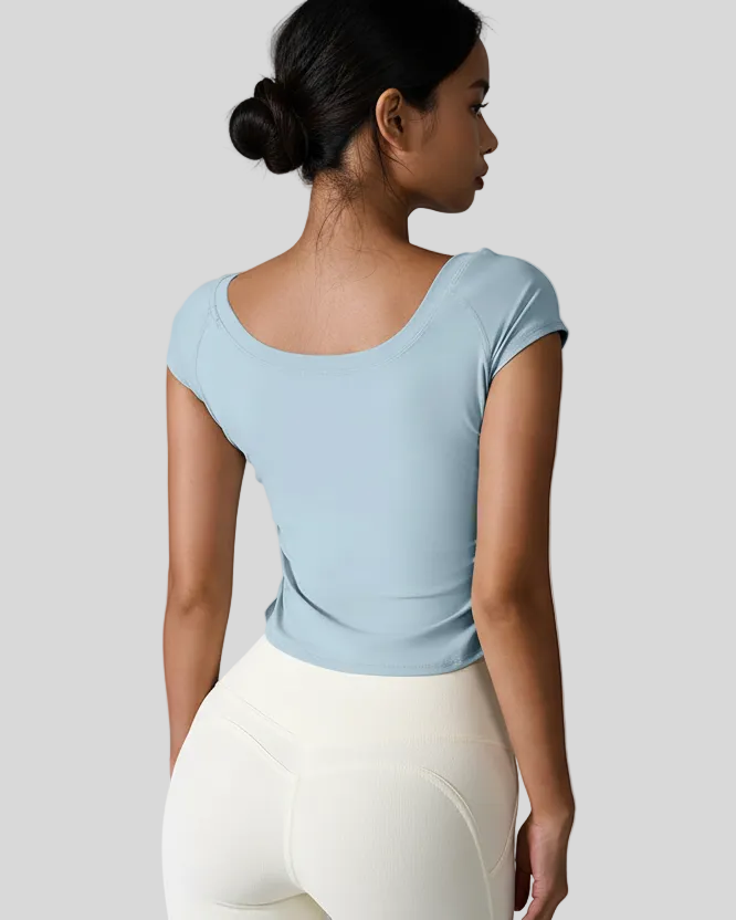 Woman wearing a light blue studioflow short sleeve active top and white leggings against a gray background