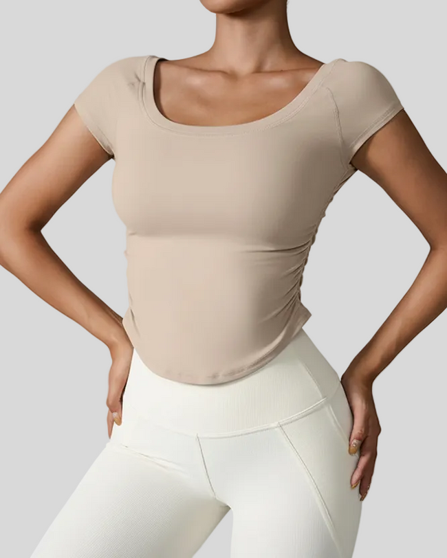 Woman wearing a beige studioflow short sleeve top and white leggings on a gray background
