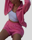 Model seated wearing Athlesi hot pink TrackEase jacket and shorts set