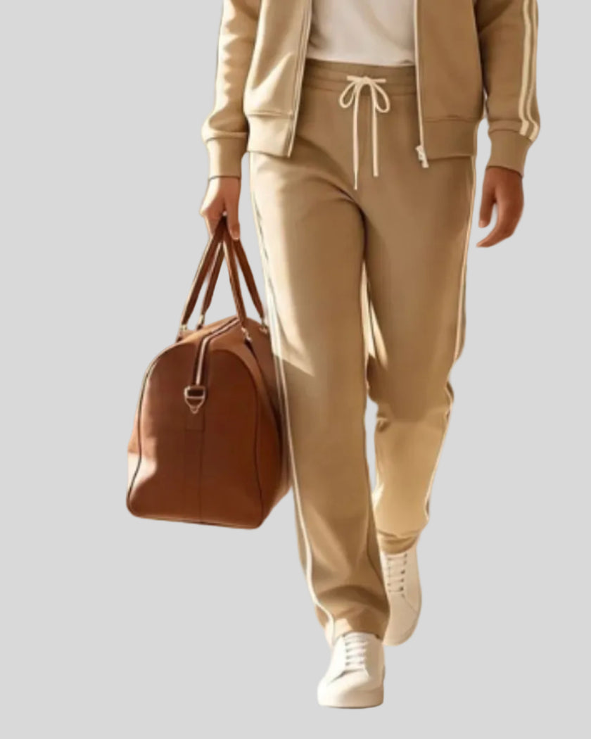 A woman walking wearing a khaki TrackLine Club sweatpants over a white top, carrying a brown leather bag.