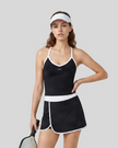 Woman wearing Athlesi TrackLine Color Block Skort in Black mid-body front view showing contrast waistband and overlapping hem