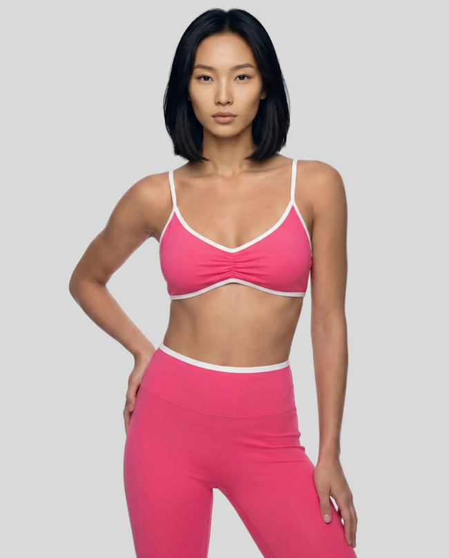 Angled front view of model wearing the Athlesi TrackLine Color Block Sports Bra in pink and white