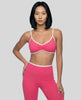 Angled front view of model wearing the Athlesi TrackLine Color Block Sports Bra in pink and white