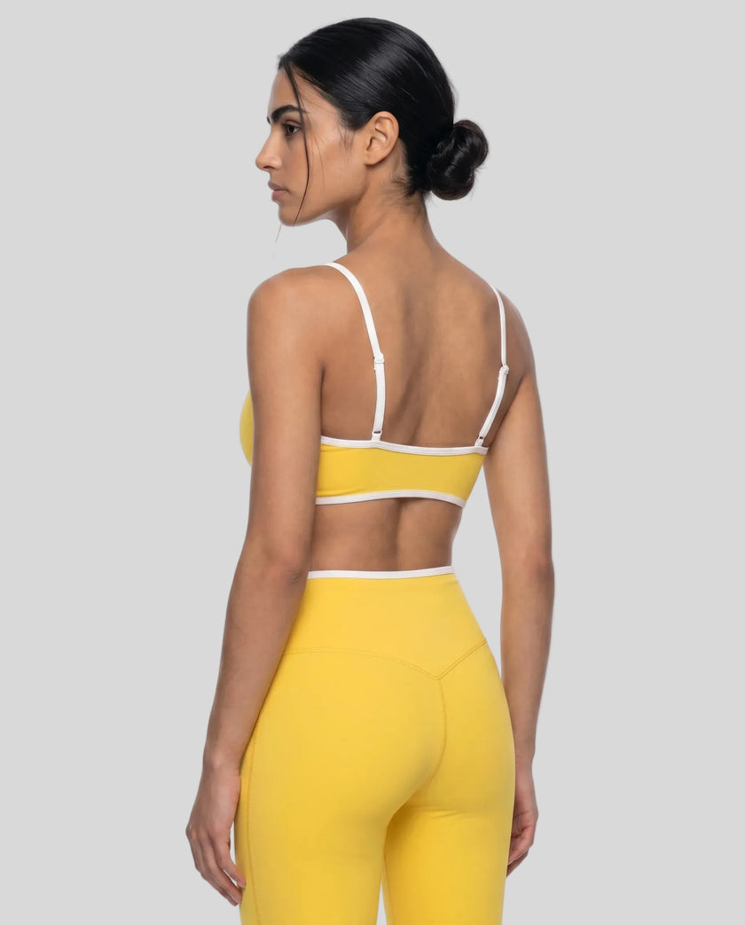Angled back view of model wearing the Athlesi TrackLine Color Block Sports Bra in yellow and white