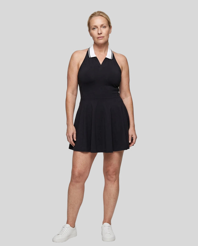 Woman modeling a black TrackLine Court Dress with a white contrast collar, paired with white sneakers