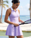 Closeup of woman stands on a beach tennis court wearing a purple TrackLine Court Dress and holding a purple and black tennis racket.
