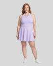 Woman modeling a purple TrackLine Court Dress, a halter-neck skater dress with a white collar, paired with white sneakers, against a light gray studio background.